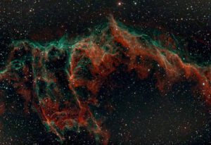 Captivating image of the Veil Nebula showing vibrant red and green hues against the starry cosmos.